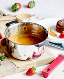 Casserole inox Casteline amovible sur une table en bois avec des fraises, un dessert et des ustensiles de cuisine.
