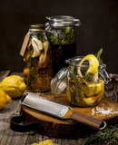 Râpe zesteur Microplane sur une planche en bois, près de bocaux d'herbes et de citrons.