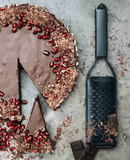 Râpe Double Tranchant Microplane à côté d'un gâteau au chocolat décoré, idéale pour les amateurs de gastronomie.