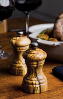 Moulin à sel en bois d'olivier Peugeot Bistro sur table en bois avec plat de légumes et vin.
