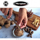 Person using a Microplane zester to grate spices into a bowl on a marble countertop.